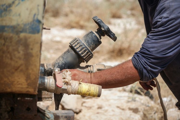 A plumber's forearm and hand working a valve on a water line with a spanner